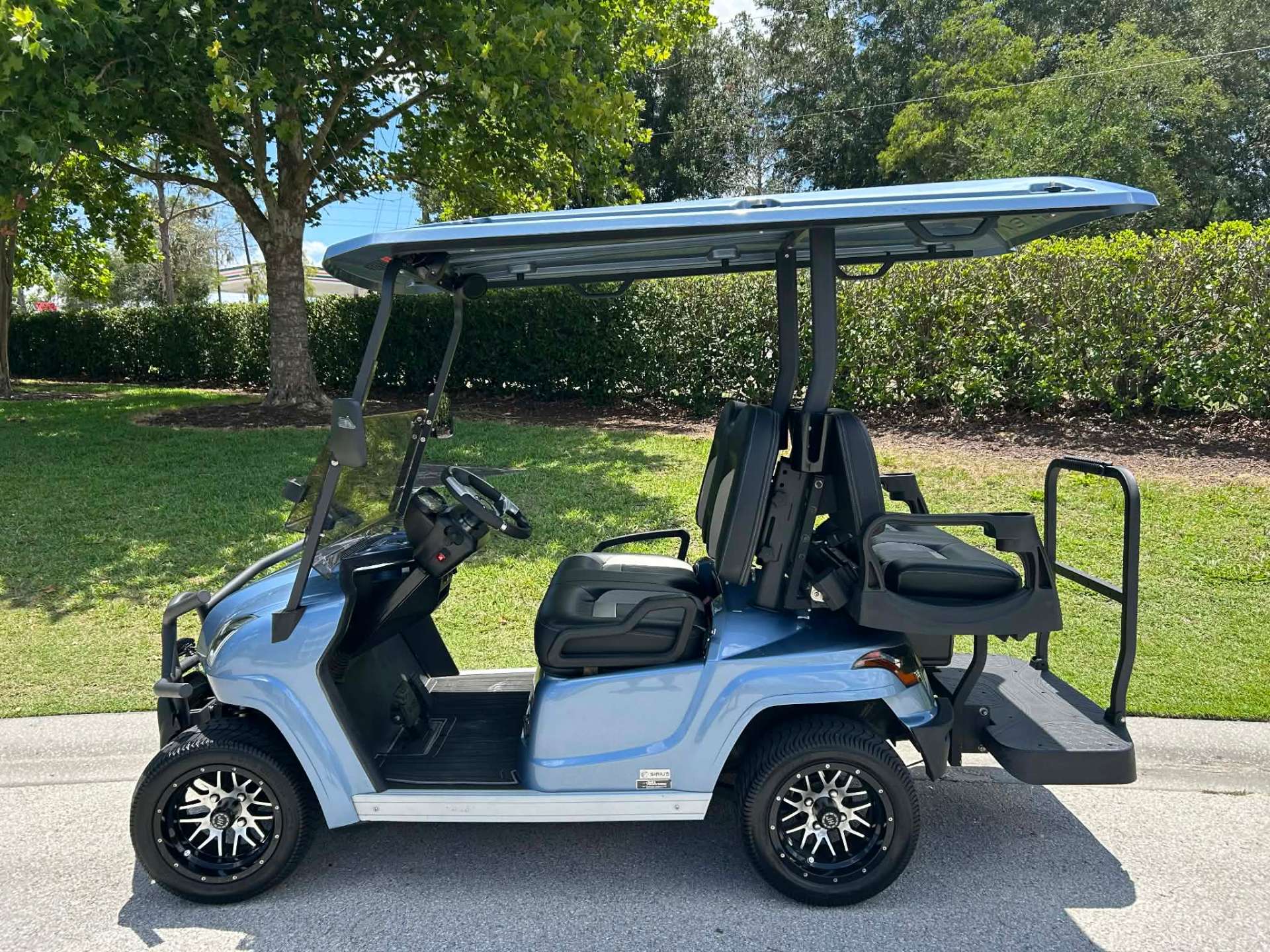 Light blue 4-seater luxury golf cart with rear-facing seat parked on a resort street